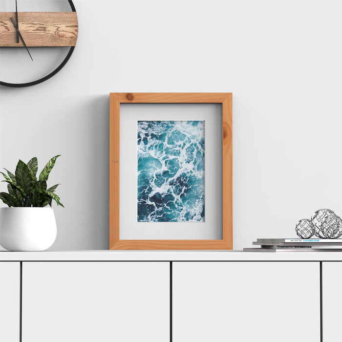Pine picture frame with white mount displaying ocean photo on a shelf with plants and decor.