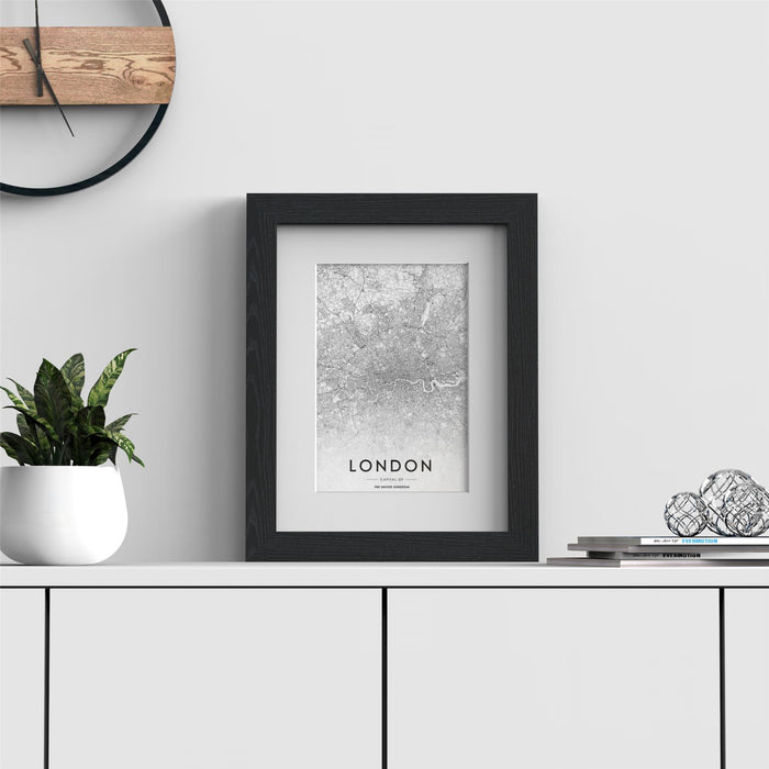 Black picture frame with white mount displaying a London map art print on a modern shelf.