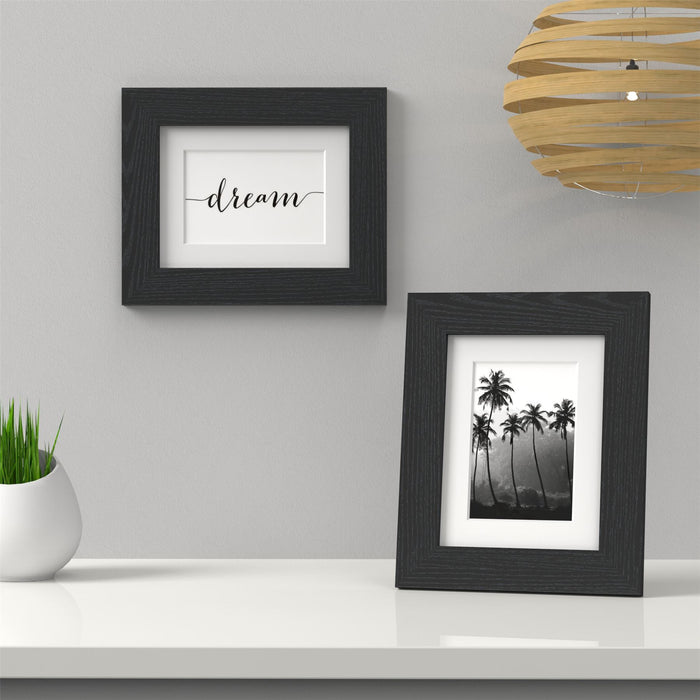 Black picture frame with white mount displaying "dream" text and palm tree artwork on a table.