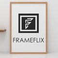 FrameFlix logo displayed in a warm oak picture and poster frame on a white wall.