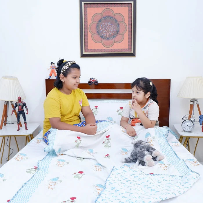 Two kids sitting on a bed with a hand block print kids dohar featuring colorful floral patterns