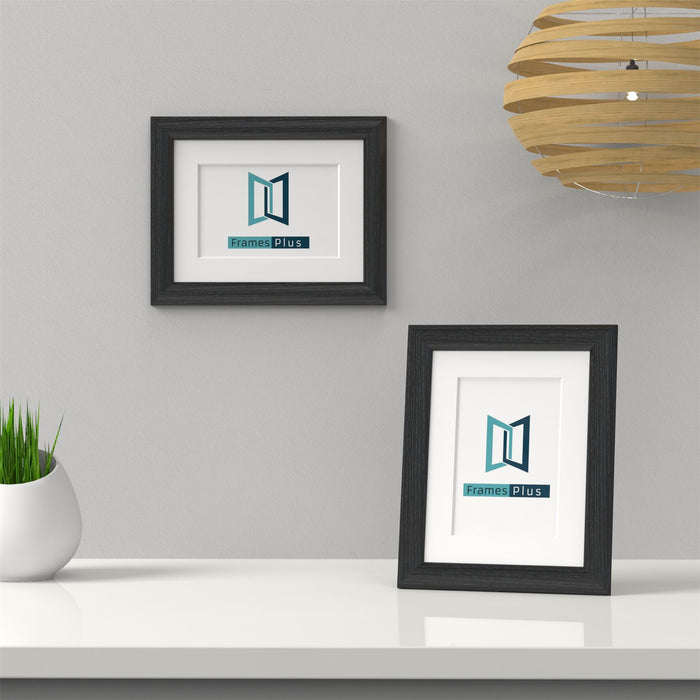 Black picture frame with white mount displaying Frames Plus logo on a table.