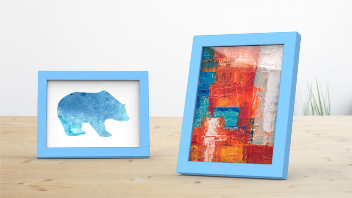 Two blue picture and poster frames displaying a bear silhouette and colorful abstract art on a wooden table.